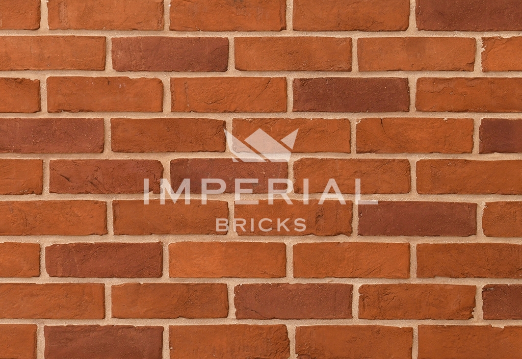 Farmhouse Orange handmade bricks shown in a wall. The bricks are orange blended with red shades, with textured creasing on the faces.